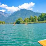 Zwei Personen paddeln auf einem See mit Bergen und Bäumen im Hintergrund.