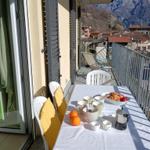Balkon mit Tisch, Stühlen und Bergblick. Frühstückszubehör und Obst sind darauf platziert.