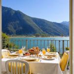 Balkon mit Tisch, Stühlen und Frühstück. Blick auf See und Berge.