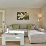 Wohnzimmer mit Ecksofa, Tisch und Wandbild. Tür und Fenster sichtbar.