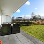 Terrasse mit Sitzgruppe, Rasen und Blick auf Bäume.