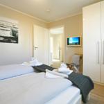 Zimmer mit Bett, Kleiderschrank und Wandbild. Fernseher an der Wand.