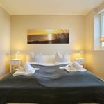 Schlafzimmer mit Bett, zwei Nachttischen und Wandbild. Fenster mit Jalousie.