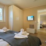 Schlafzimmer mit Bett, Kleiderschrank und Fernseher. Durchgang zu weiterem Raum.