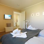 Schlafzimmer mit Bett, Handtüchern, Fernseher und Türen.