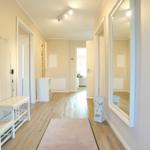 Flur mit Holzboden, Spiegel und Sitzbank. Wanddekoration und Teppich sichtbar.