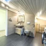 Badezimmer mit Waschmaschine, Toilette und Spiegel. Holzoptik und Steinfliesen.