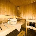 Sauna mit Holzbank, Eimer und Ölflasche. Heizung unter Holzgestell.
