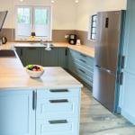 Modern kitchen with island, wooden surfaces, and stainless steel refrigerator.