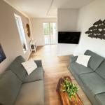 Living room with two sofas, wooden table, and TV. Corridor to terrace.