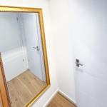 Hallway with gold-framed mirror and white doors on light wood floor