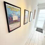 Hallway with wall pictures and wooden floor. Door leads outside.