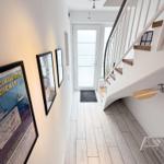 Hallway with wooden floor, staircase, and wall art. Door to outdoor area.