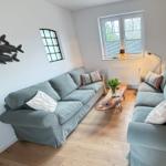 Living room with two sofas, wooden floor, and windows. Table with flowers and wall decoration.