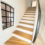 Wooden staircase with white railing and black-framed window in the background.