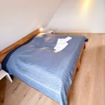 Bedroom with wooden floor and sloped ceiling. Bed with blue quilt and white pillows.