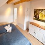 Bedroom with bed, wooden floor, and wall art. Visible ceiling beams and cabinet.