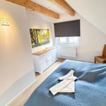 Bedroom with sloped ceiling, wooden beams, bed, and dresser.