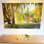 Wall picture shows a lake with trees and church tower. White flowers lie on the table.