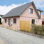 A pink house with gray roof and wooden fence. Gravel yard with shrubs.