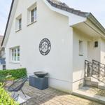 Wohnhaus mit Terrasse, Garten und Eingangstreppe. Außenwand mit Logo.