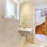 Badezimmer mit Waschbecken, Spiegel und Fenster. Treppe führt in den Flur.