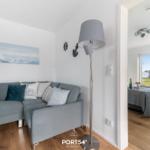 Wohnzimmer mit Sofa und Lampen. Durchgang zur Schlafzimmer mit Bett und Fenster.