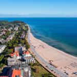 Strandpromenade mit Hotels und Strand. Blick aufs Meer und grüne Landschaft.