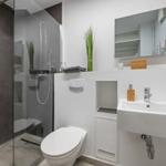 Badezimmer mit Dusche, Waschbecken und Toilette. Weiße Wände und graue Fliesen.