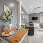 Esszimmer mit Tisch, Stühlen und Blumen. Wohnzimmer mit Sofa und Fernseher.