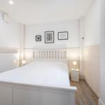 Schlafzimmer mit weißem Bett, zwei Nachttischen und Wandbildern.