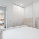 Schlafzimmer mit Bett und Blick in Wohnbereich mit Küchenzeile.