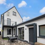 Wohnhaus mit Terrasse, Tisch und Stühlen. Schwarze Fensterrahmen und Tür. Weiße Fassade.