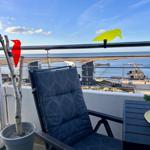 Terrasse mit Sessel, Tisch und Blick auf Meer und Hafen.