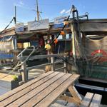 Holztisch und -bänke vor Fischerhütte mit Netzen und Schildern