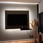 TV an der Wand mit eingebauter Beleuchtung und dekorativen Pflanzen im Vordergrund.