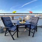 Terrasse mit Tisch, zwei Stühlen und Meerblick. Auf dem Tisch steht eine Flasche Champagner.