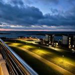 Abendansicht vom Balkon mit Blick auf beleuchtete Grünfläche und Meeresufer.