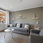 Wohnzimmer mit grauem Sofa, weißen Regalen und Blick auf Gebäude.