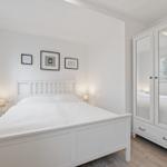 Schlafzimmer mit weißem Bett, Kleiderschrank und Fenster.