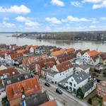 Panoramablick auf einen Fluss mit Häusern und Booten am Ufer.