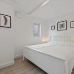 Ein Schlafzimmer mit weißem Bett, Holzboden und Wandbildern.