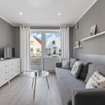 Wohnzimmer mit Sofa, Couchtisch und Fernseher. Balkon mit Blick auf Gebäude.