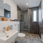 Badezimmer mit Dusche, Waschbecken und Toilette. Holzoptik und dunkle Wandfarbe.