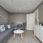 Wohnzimmer mit grauem Sofa, weißem Tisch und Schrank. Holzfußboden und Wanddekoration.