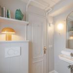 Badezimmer mit Spiegel, Waschbecken und Toilette. Regal mit Büchern und Lampe.