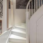 Weiße Treppe mit geschwungenem Geländer und Wandbildern an den Wänden.