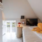 Schlafzimmer mit Dachschräge, Bett, Fernseher und Fenster zur Außenterrasse.