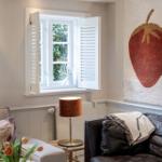 Ein Wohnzimmer mit Fenster, Schiebetüren, Ledersofa und Wandbild mit Erdbeere.