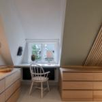 Schlafzimmer mit Schreibtisch, Stuhl und Holzschränken unter Dachschrägen.